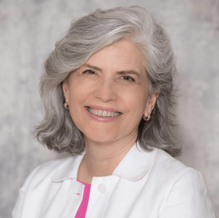 Headshot of Maria wearing a white jacket and pink top